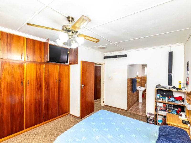 Bedroom featuring extensive built-in wooden cabinetry, a ceiling fan, and direct access to an en-suite bathroom with tiled finishes.