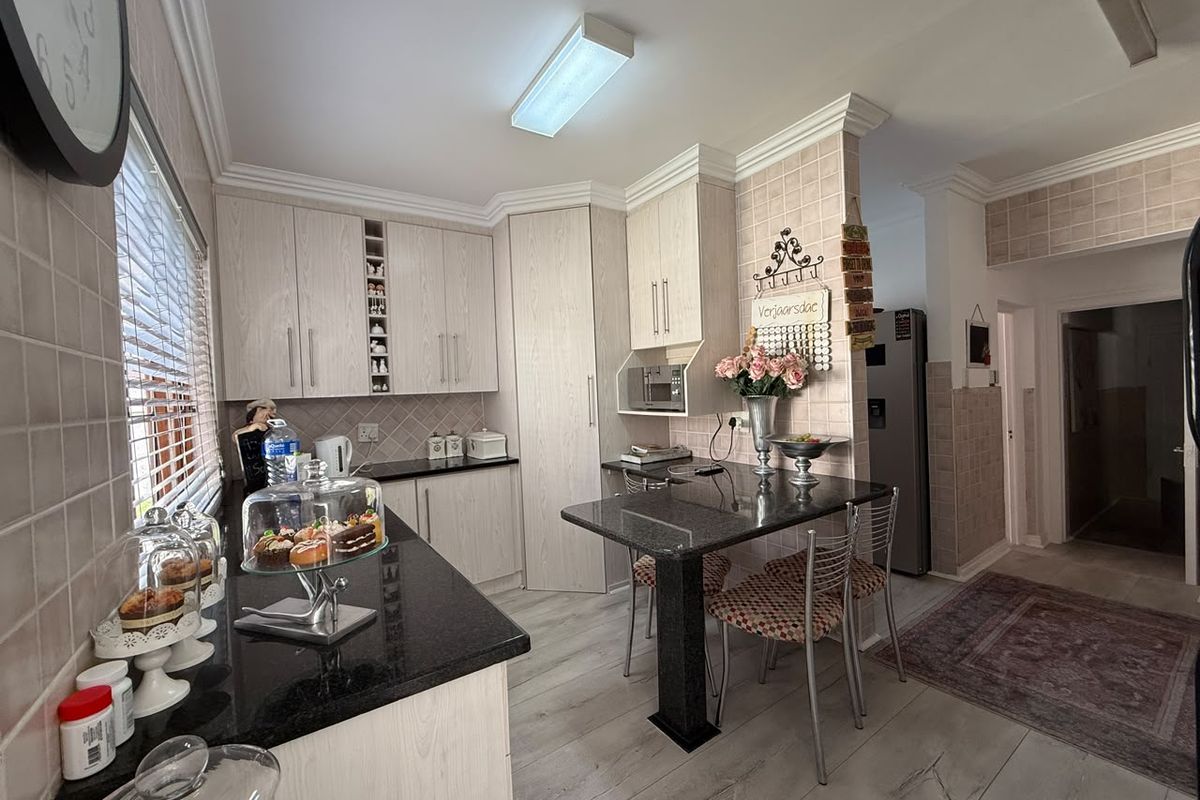 A functional kitchen featuring light wood-grain cabinetry, dark granite countertops, tiled backsplash, and a built-in breakfast nook area.