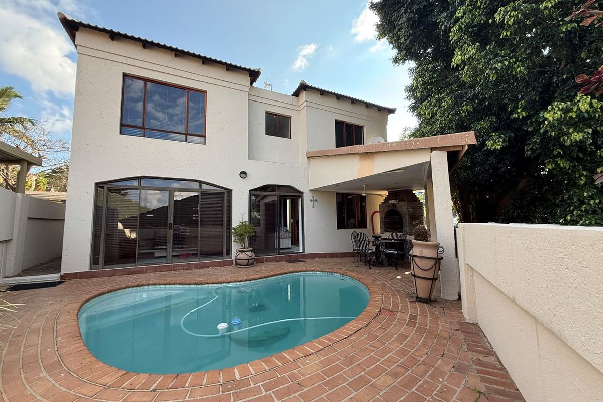 Rear exterior view featuring a swimming pool, brick-paved patio area, and a covered entertainment space with a built-in braai.