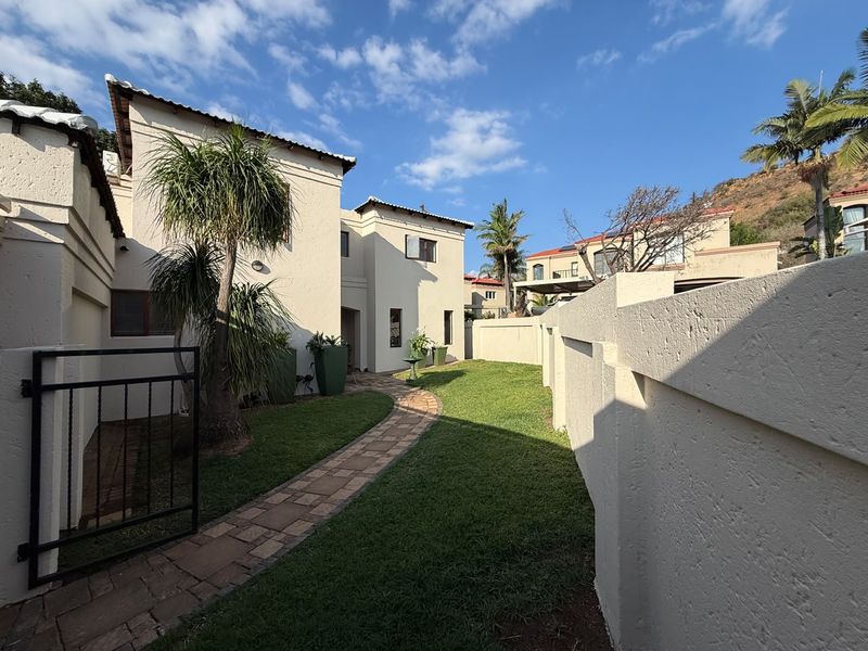 A well-maintained rear garden area featuring a paved walkway, lush lawn, and secure boundary walls, providing a private outdoor space.
