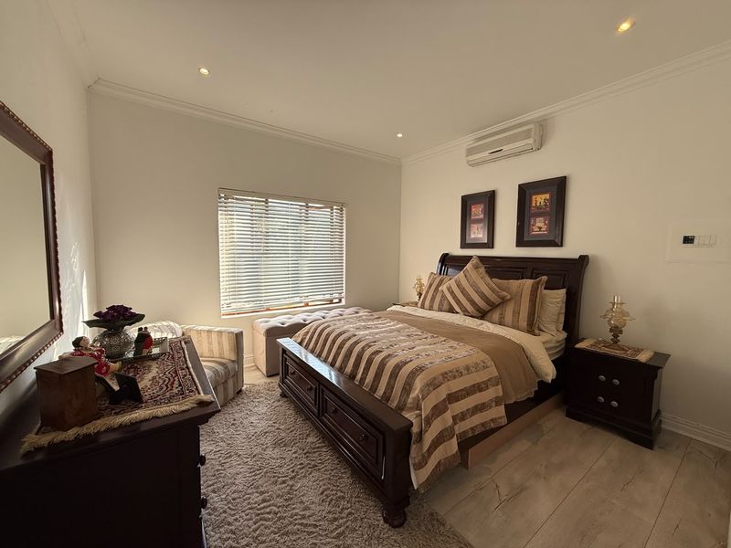 A well-maintained bedroom featuring laminate flooring, recessed downlighting, coved cornicing, and a wall-mounted air conditioning unit.