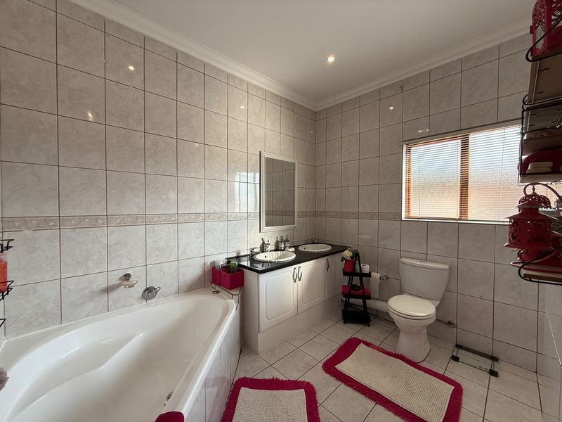 A well-maintained bathroom featuring a corner bathtub, dual basin vanity, and full-height wall tiling with neutral finishes.