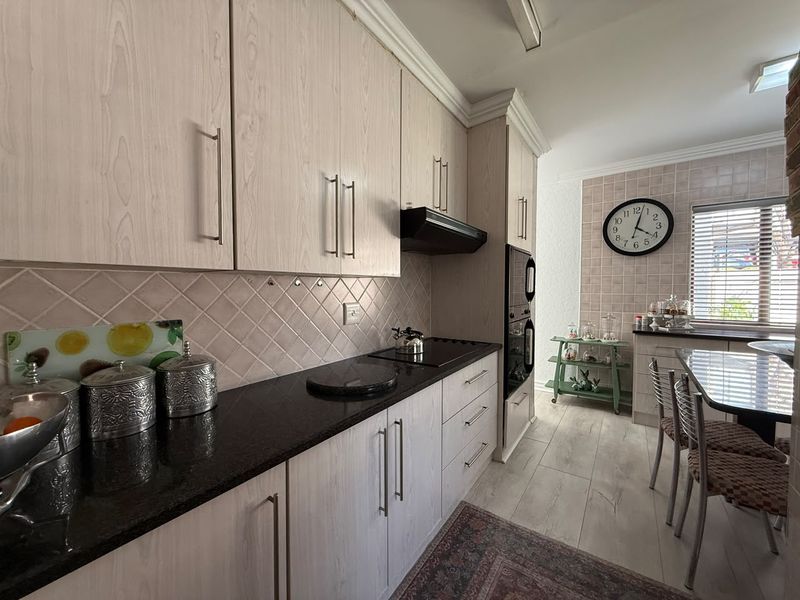 A functional kitchen featuring light wood-grain cabinetry, dark granite countertops, built-in oven, and a tiled backsplash with a dedicated dining area.