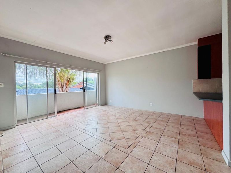Open plan living area featuring tiled flooring, sliding glass doors leading to a balcony, and a partial view of the kitchen cabinetry.
