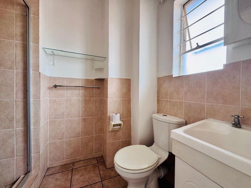 A functional bathroom featuring a shower enclosure, toilet, and vanity basin with tiled walls and flooring, providing a practical layout.