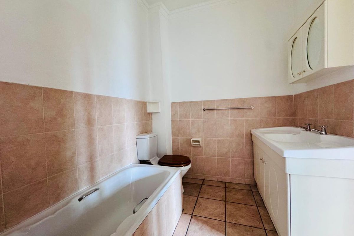 A functional bathroom featuring a built-in bathtub, vanity cabinet with integrated sink, and tiled wall and floor finishes.
