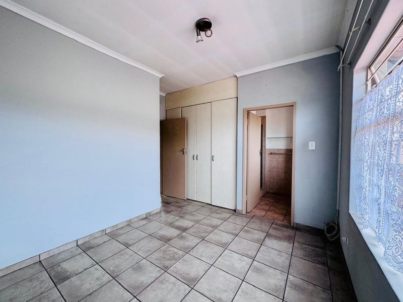 A functional bedroom featuring built-in cupboards, tiled flooring, and direct access to an en-suite bathroom.