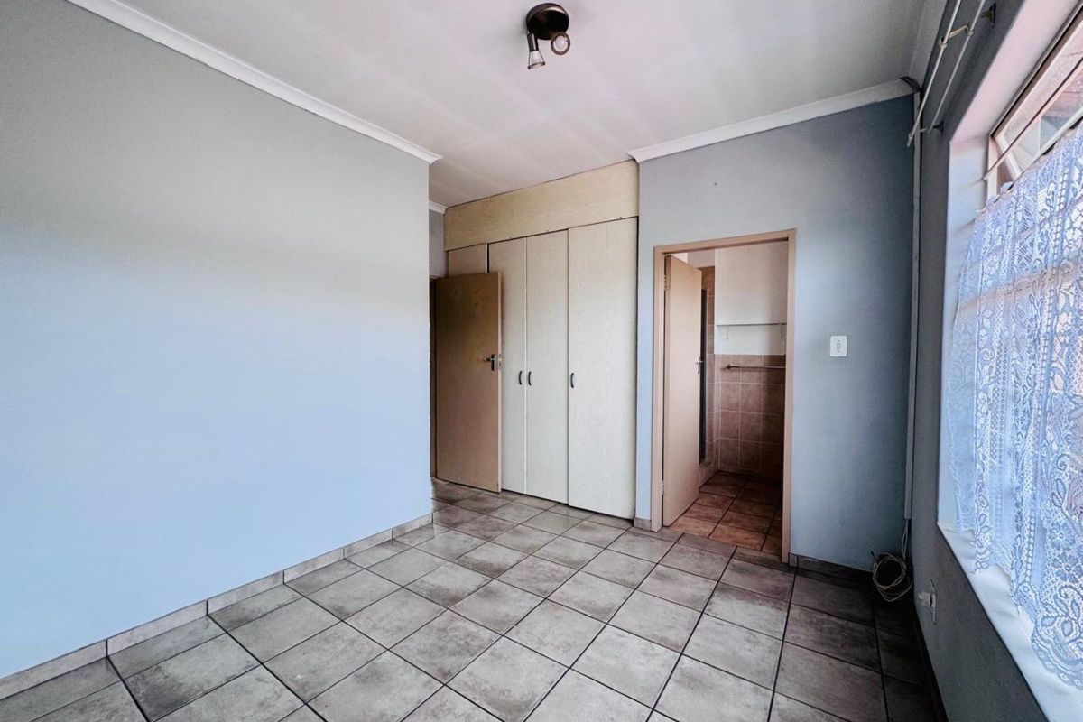 A functional bedroom featuring built-in cupboards, tiled flooring, and direct access to an en-suite bathroom.