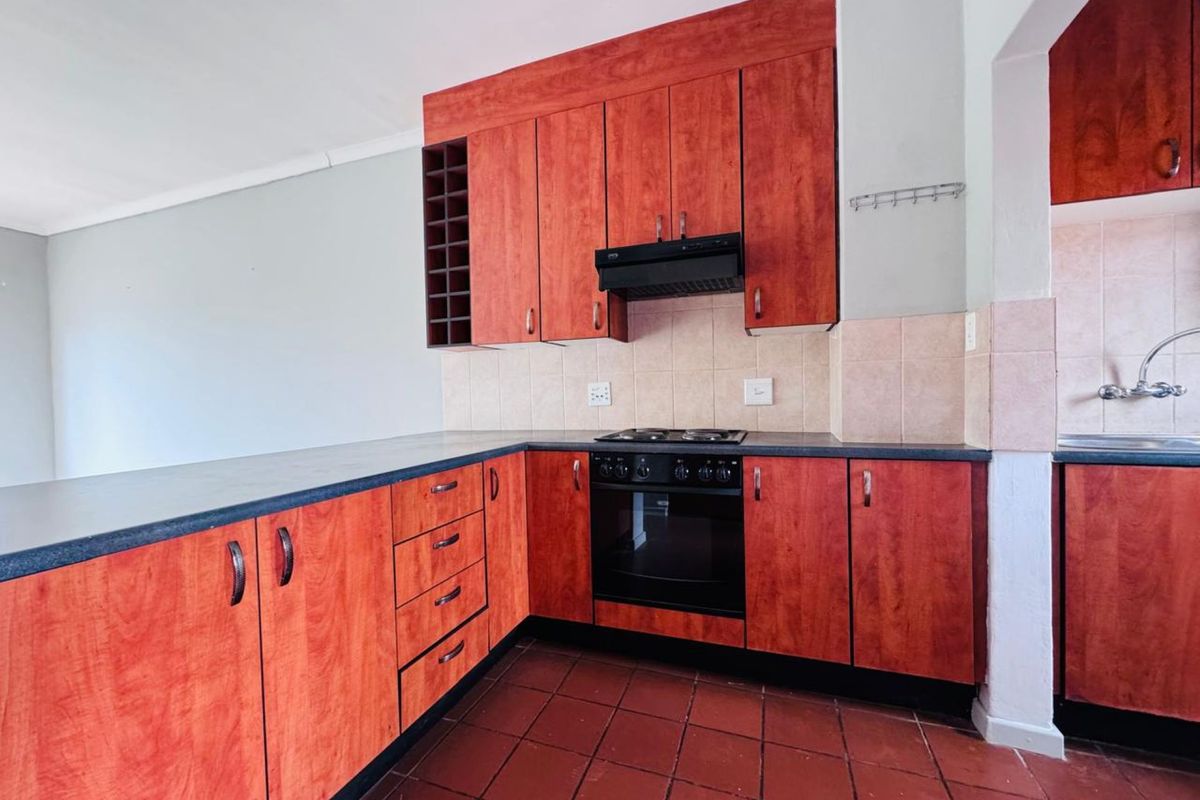 A functional kitchen featuring wood-toned cabinetry, a built-in oven and hob, tiled backsplash, and dark countertops, with an adjacent scullery area.