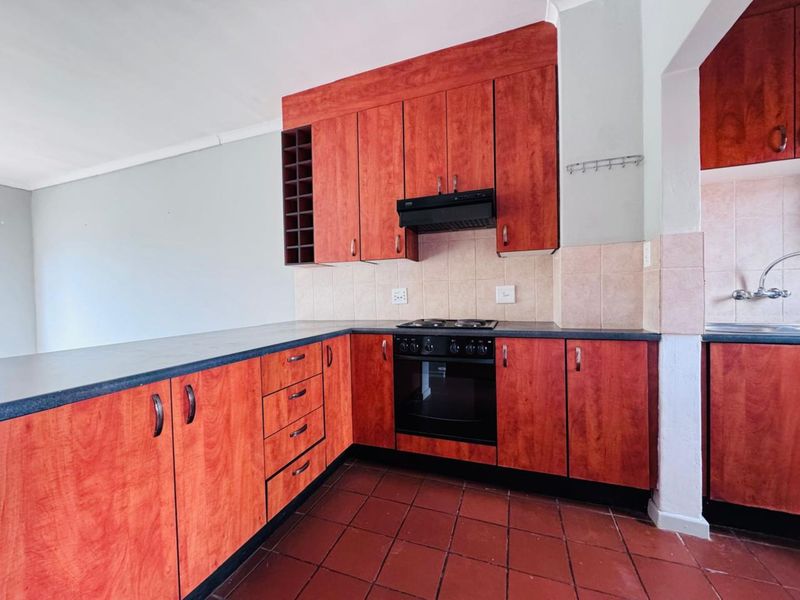 A functional kitchen featuring wood-toned cabinetry, a built-in oven and hob, tiled backsplash, and dark countertops, with an adjacent scullery area.