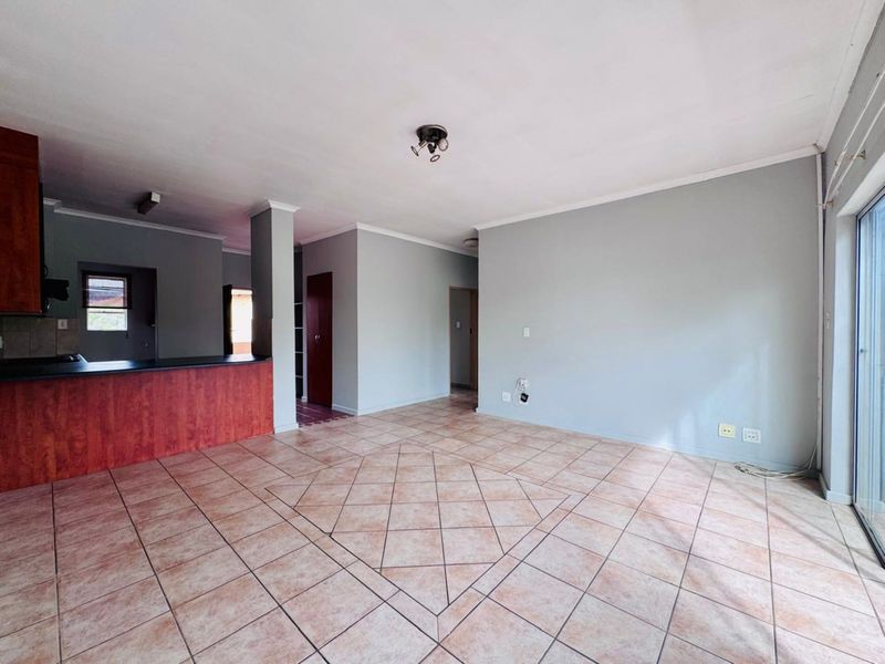 An open-plan living and kitchen area featuring tiled flooring, a breakfast counter, and sliding glass doors leading to an outdoor space.