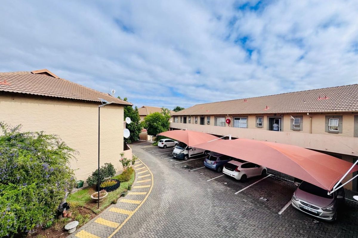 An elevated view of the apartment complex parking area featuring paved driveways and covered shade-cloth parking bays.