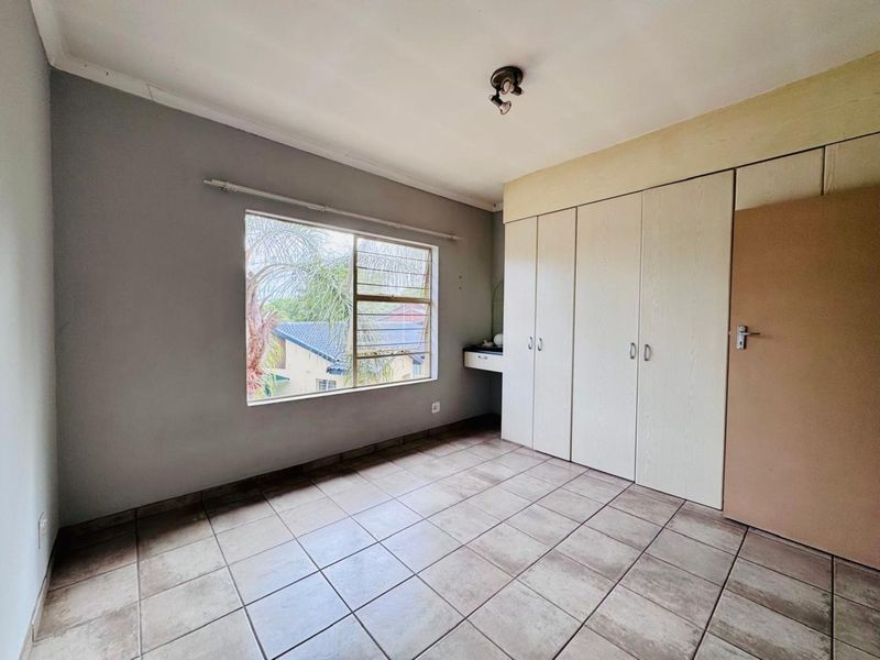 A bedroom featuring built-in cupboards, tiled flooring, and a large window providing natural light.