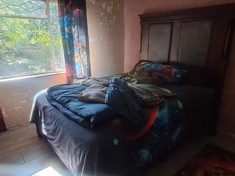 A bedroom featuring a window with natural light, requiring significant wall repairs and cosmetic updates to improve the overall condition.