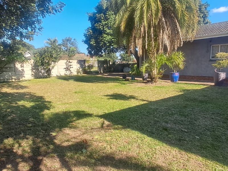 A spacious rear garden featuring a well-maintained lawn, mature trees, and a precast concrete boundary wall, adjacent to the rear facade of the house.