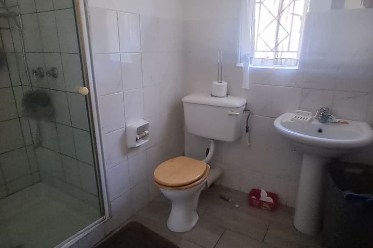 A functional bathroom featuring a shower enclosure, pedestal basin, and toilet with tiled wall finishes and security bars on the window.