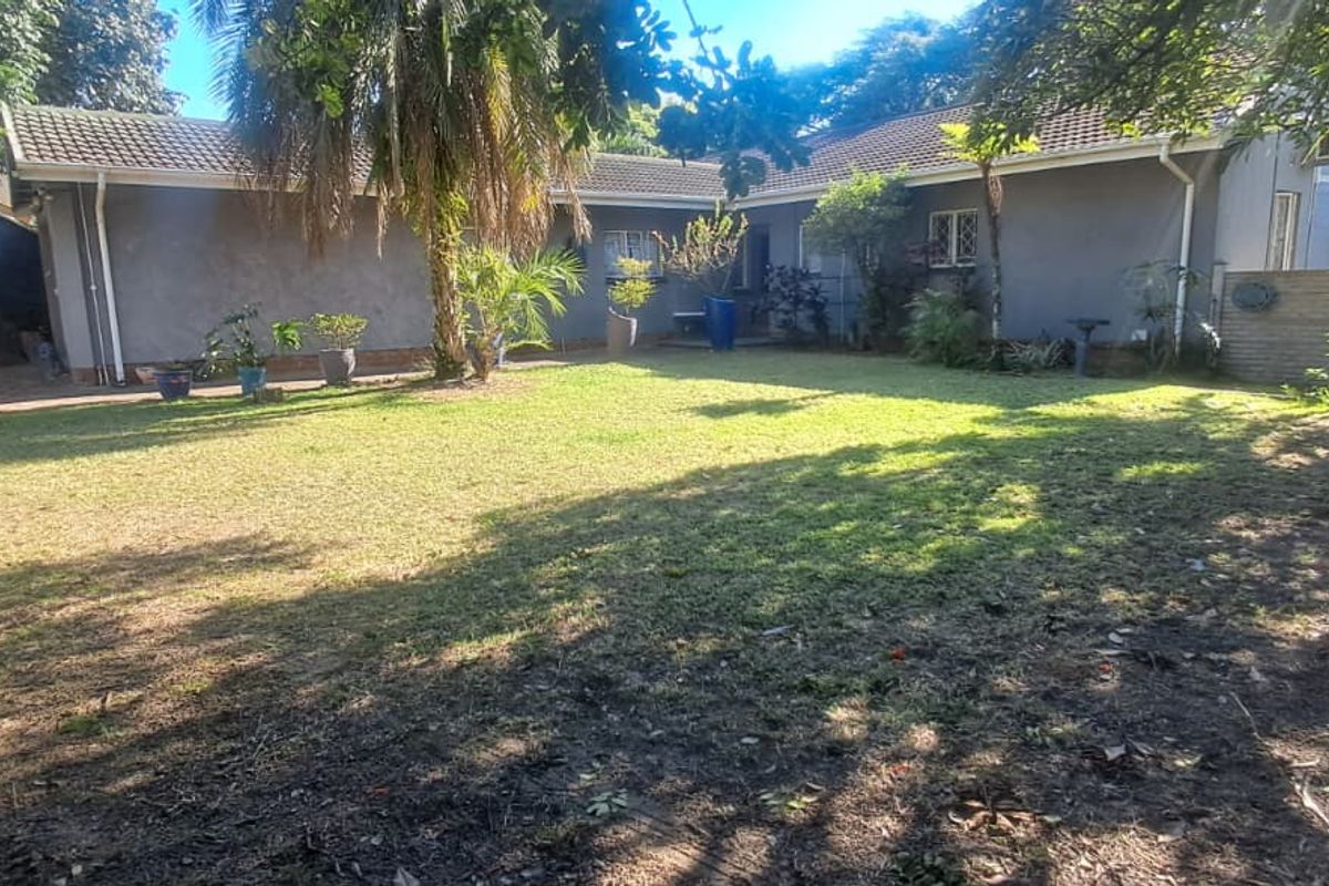 A view of the rear garden and the back elevation of the house, featuring a lawn and established trees.
