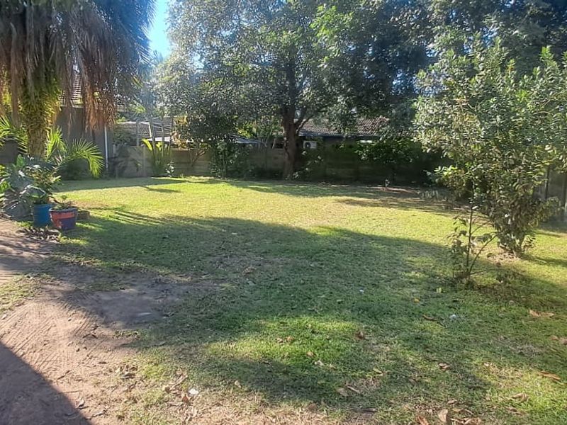 A spacious rear garden featuring a paved patio area, established trees, and a secure precast concrete boundary wall.