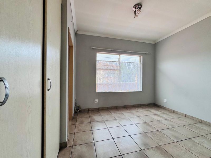 A vacant bedroom featuring neutral wall tones, tiled flooring, and built-in cupboard storage.