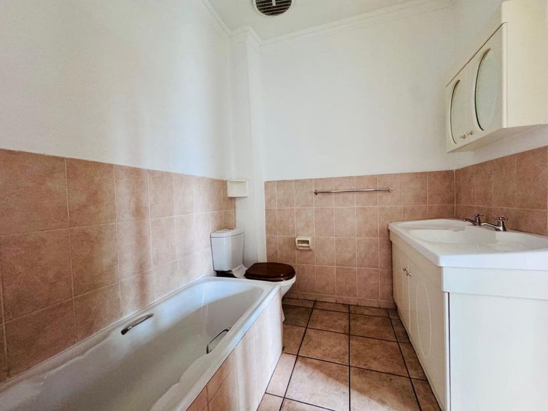 A functional bathroom featuring a built-in bathtub, vanity cabinet with integrated sink, and tiled wall and floor finishes.