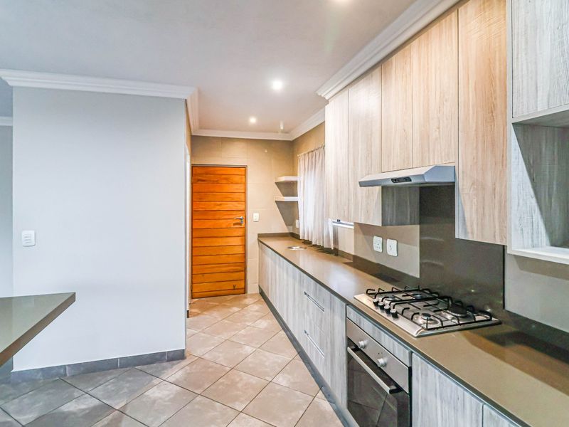 Modern kitchen featuring light wood-grain cabinetry, stone countertops, a gas hob with extractor fan, and tiled flooring.