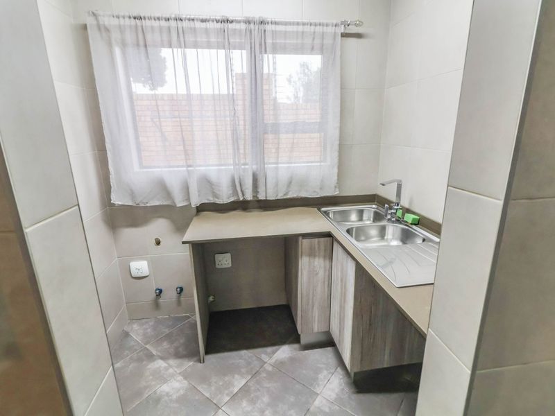 A functional laundry area featuring tiled finishes, built-in cabinetry, and a stainless steel sink with dedicated plumbing connections for appliances.