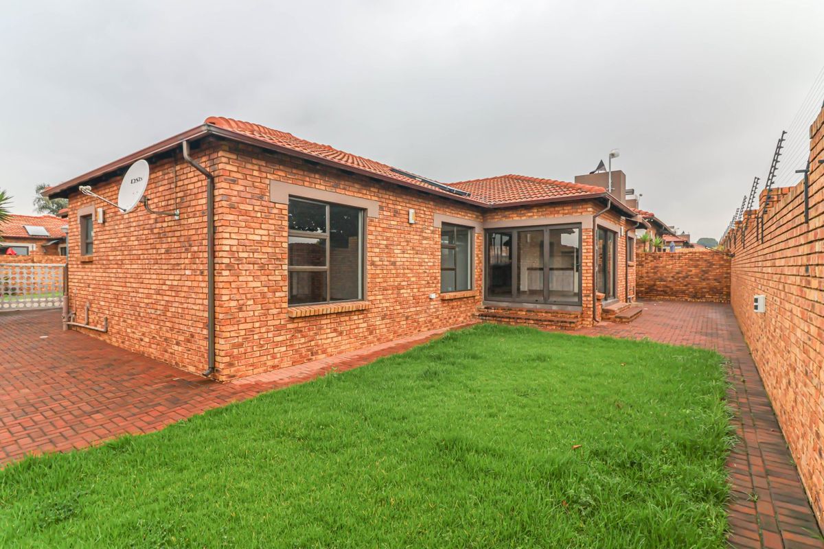 Rear view of the cluster home featuring a face-brick exterior, tiled roof, paved patio area, and a private garden with perimeter wall and electric fencing.