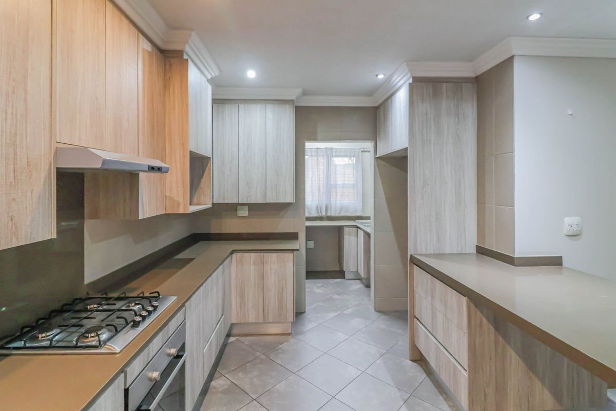 Modern kitchen featuring light wood-grain cabinetry, stone countertops, gas hob, and an integrated oven, with an adjoining scullery area.