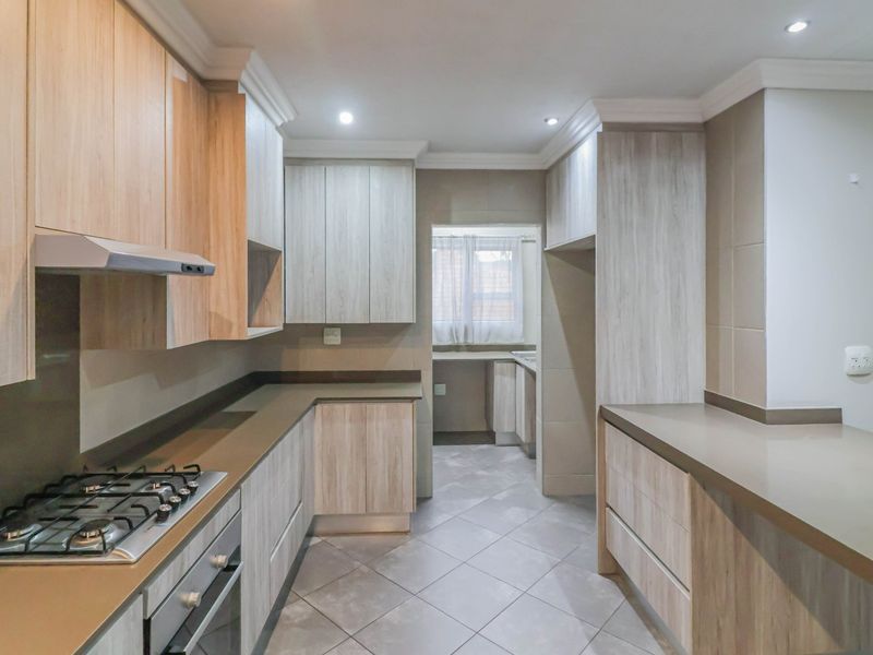 Modern kitchen featuring light wood-grain cabinetry, stone countertops, gas hob, and an integrated oven, with an adjoining scullery area.