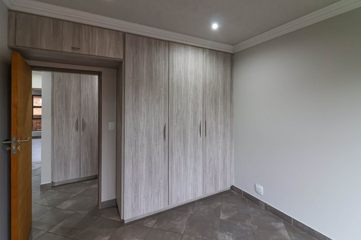 A clean, empty bedroom featuring modern wood-grain built-in cupboards, tiled flooring, and recessed ceiling lighting.