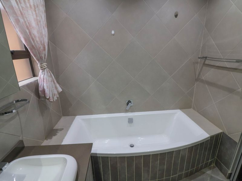 A well-maintained bathroom featuring a built-in bathtub with tiled surround, a vanity basin, and modern chrome fixtures.