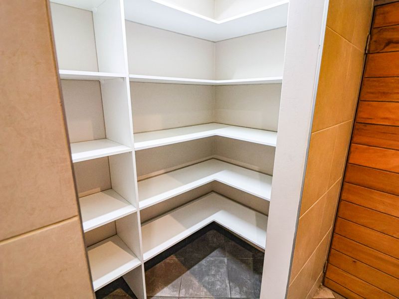 A clean, walk-in pantry or scullery area featuring white built-in shelving and tiled flooring, providing ample storage space.