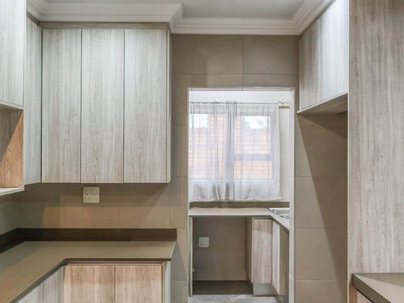 A clean and modern scullery area featuring light wood-grain cabinetry, stone countertops, and a functional sink area with tiled splashbacks.