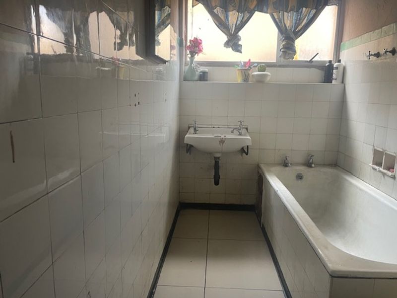 A dated bathroom featuring a wall-mounted basin and a built-in bathtub with full-height ceramic wall tiling.
