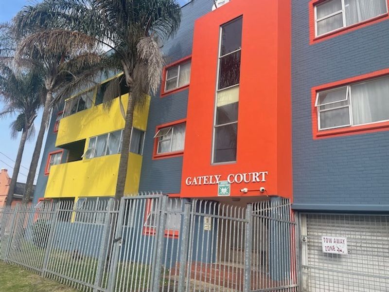 Front elevation of Gately Court apartment building featuring a multi-colored brick facade, security fencing, and gated entrance.