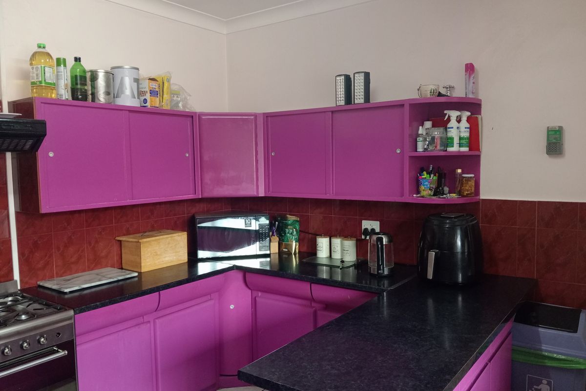 A functional kitchen featuring vibrant purple cabinetry, dark laminate countertops, and a tiled backsplash, providing ample storage and workspace.