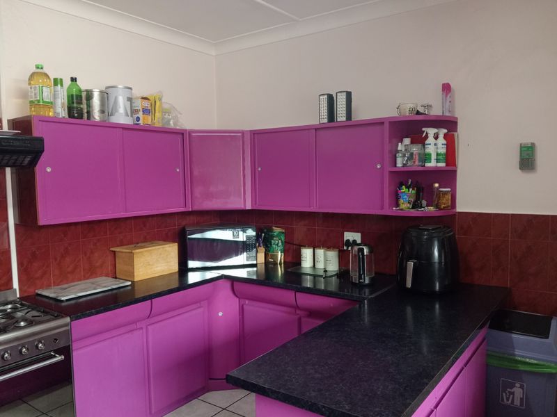 A functional kitchen featuring vibrant purple cabinetry, dark laminate countertops, and a tiled backsplash, providing ample storage and workspace.