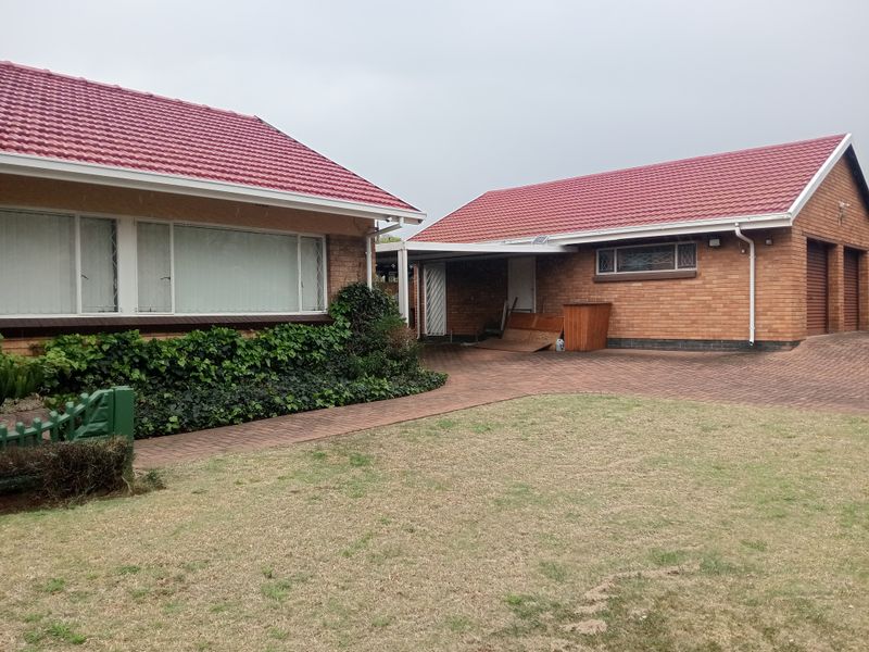 Front view of a brick house featuring a tiled roof, paved driveway, double garage, and attached carport with a front lawn.