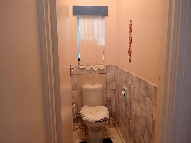 A compact guest bathroom featuring ceramic wall and floor tiling, a standard toilet, and a window for natural light.