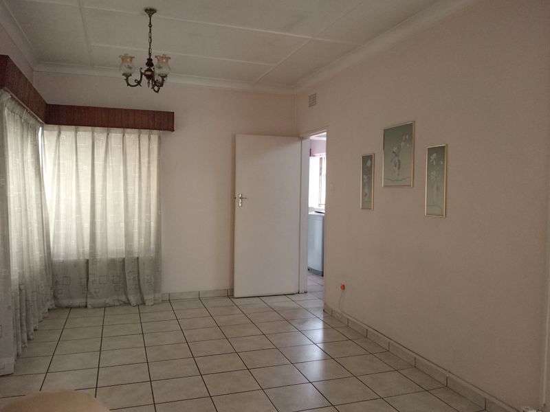 A bright, empty living room featuring neutral tiled flooring, coved cornicing, and a classic ceiling light fixture, offering a clean canvas for interior design.