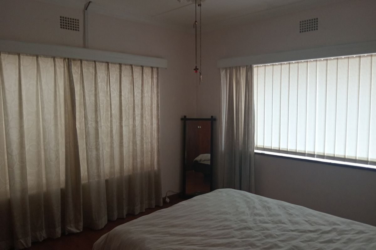 A bedroom featuring dual window treatments with vertical blinds and curtain tracks, complemented by a ceiling fan and neutral wall finishes.