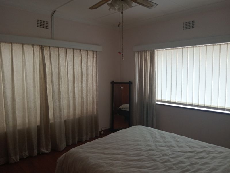A bedroom featuring dual window treatments with vertical blinds and curtain tracks, complemented by a ceiling fan and neutral wall finishes.