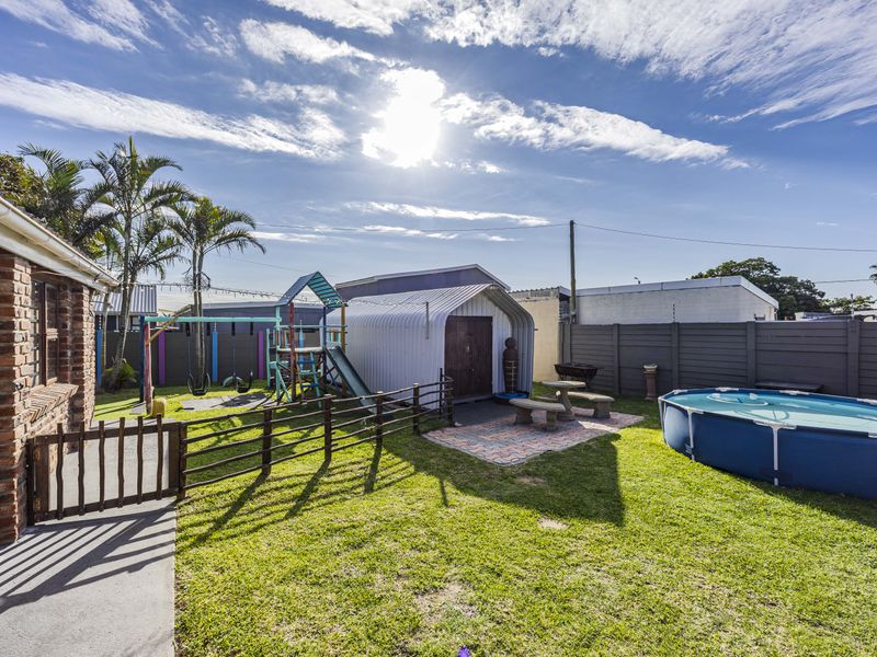 A rear garden area featuring a lawn, paved section, perimeter fencing, and brick exterior wall of the house.