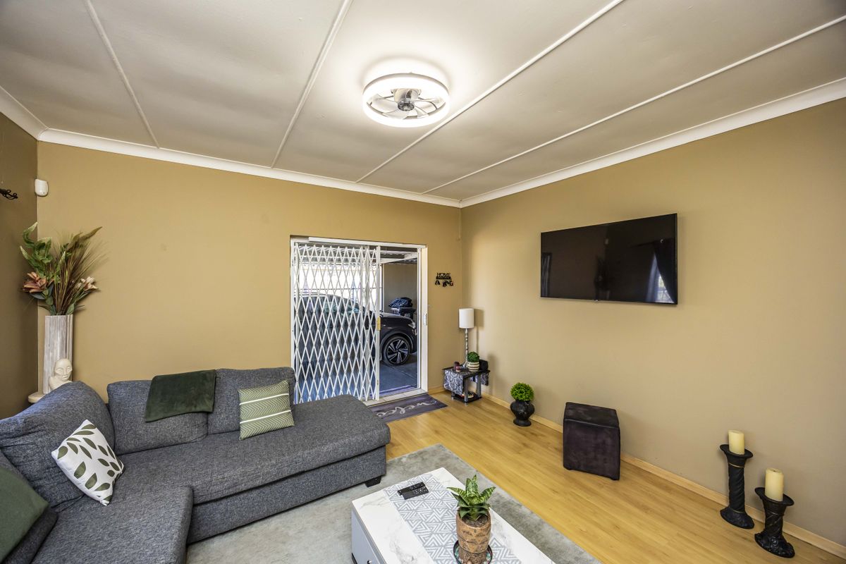 A comfortable living room featuring laminate flooring, a ceiling fan, and a security gate leading to the exterior.