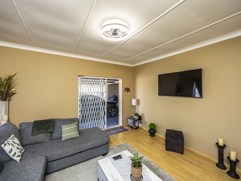 A comfortable living room featuring laminate flooring, a ceiling fan, and a security gate leading to the exterior.