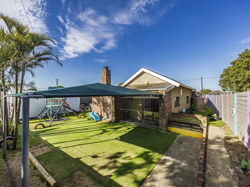 Rear exterior view featuring a brick chimney, shade sail covering an artificial lawn area, concrete pathway, and perimeter boundary wall.