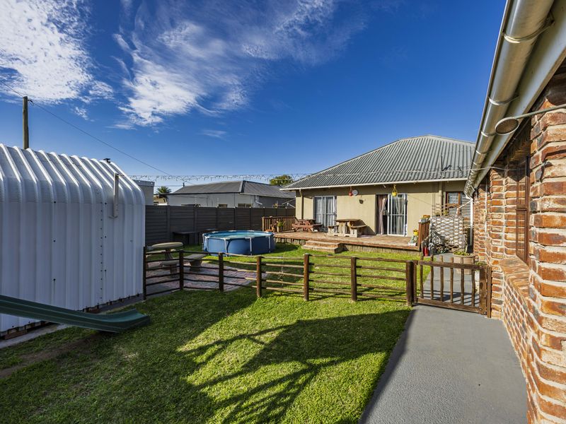 Rear exterior view featuring a brick facade, timber decking, lawn area, and perimeter fencing, providing a functional outdoor space.