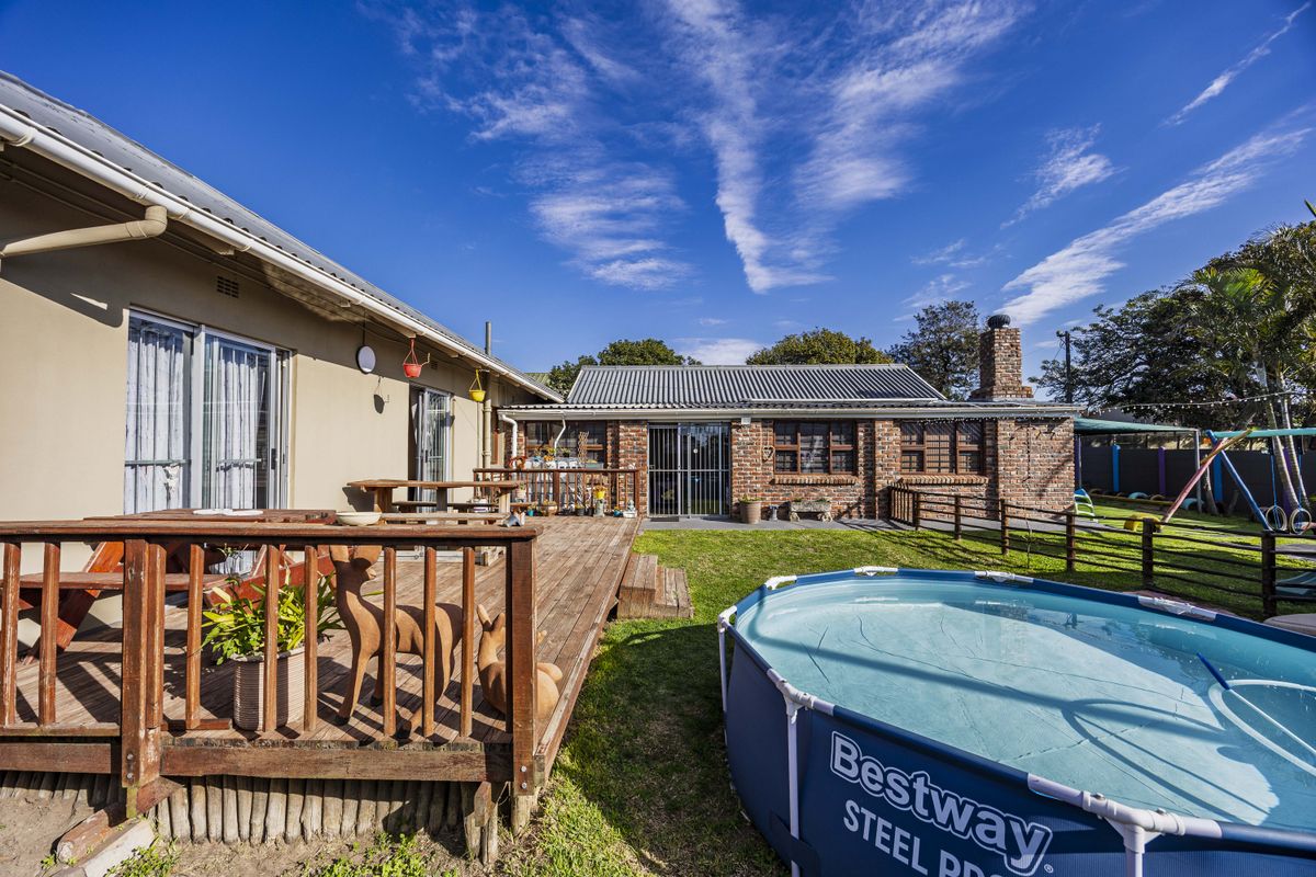 Rear exterior view featuring a wooden deck, a brick outbuilding with a corrugated roof, and a spacious garden area.