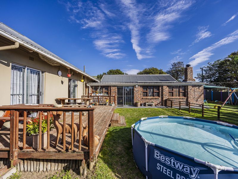 Rear exterior view featuring a wooden deck, a brick outbuilding with a corrugated roof, and a spacious garden area.