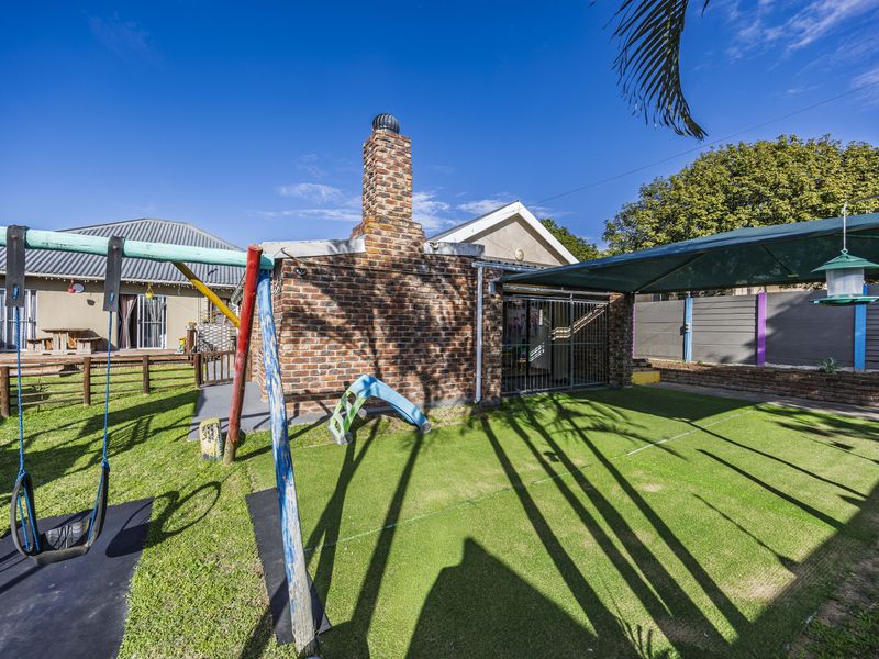 A rear garden area featuring an artificial lawn, a brick chimney structure, and a shaded outdoor space with boundary walling.